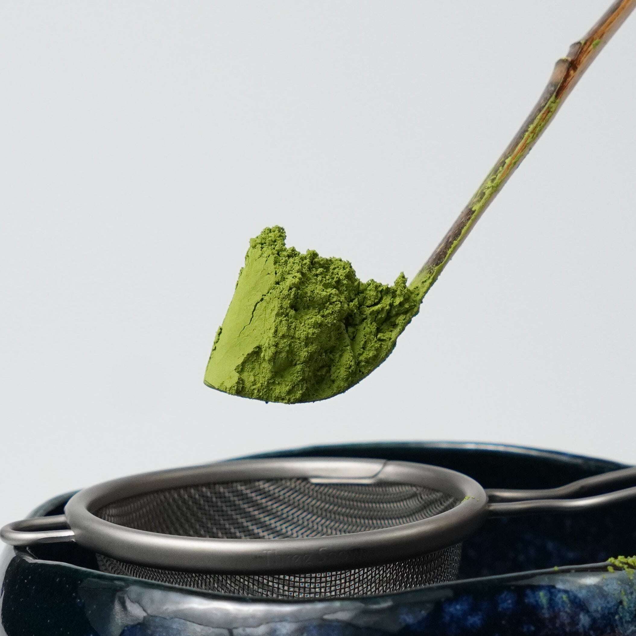 Matcha scoop with green Koharu no Shiro matcha powder by Yamada Chaya over a blue ceramic bowl on a light gray background