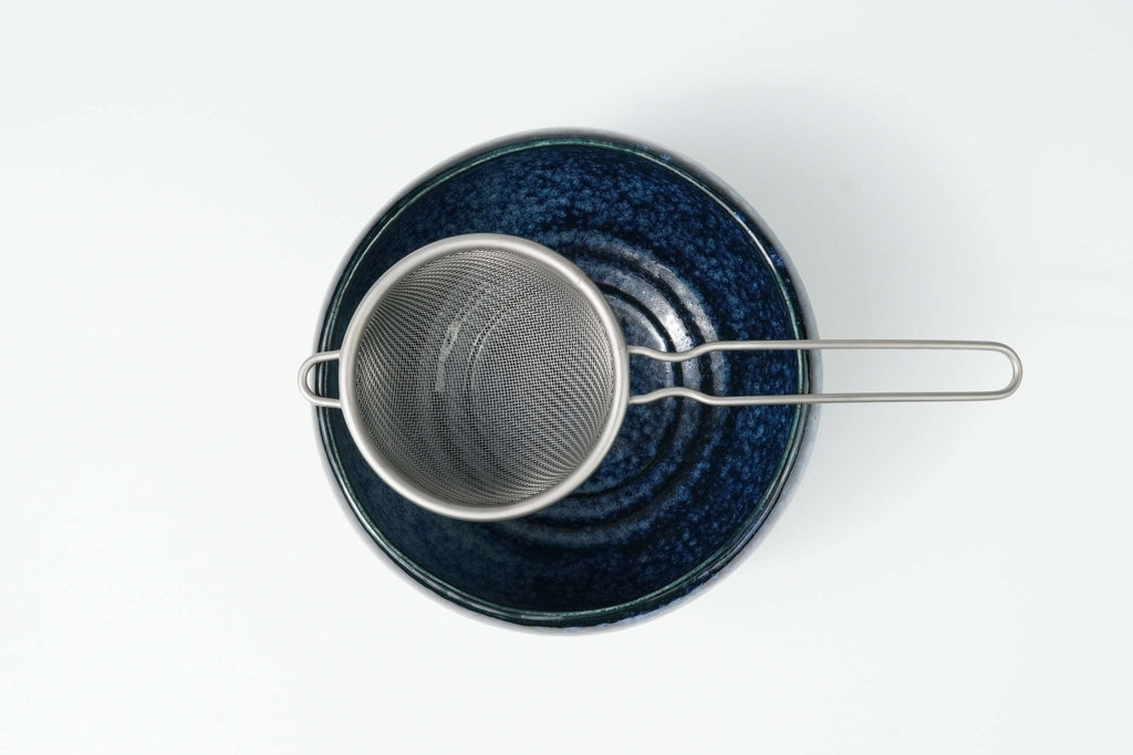 Blue speckled matcha bowl with a metal matcha sieve on a white background
