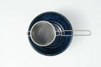 Blue speckled matcha bowl with a metal matcha sieve on a white background