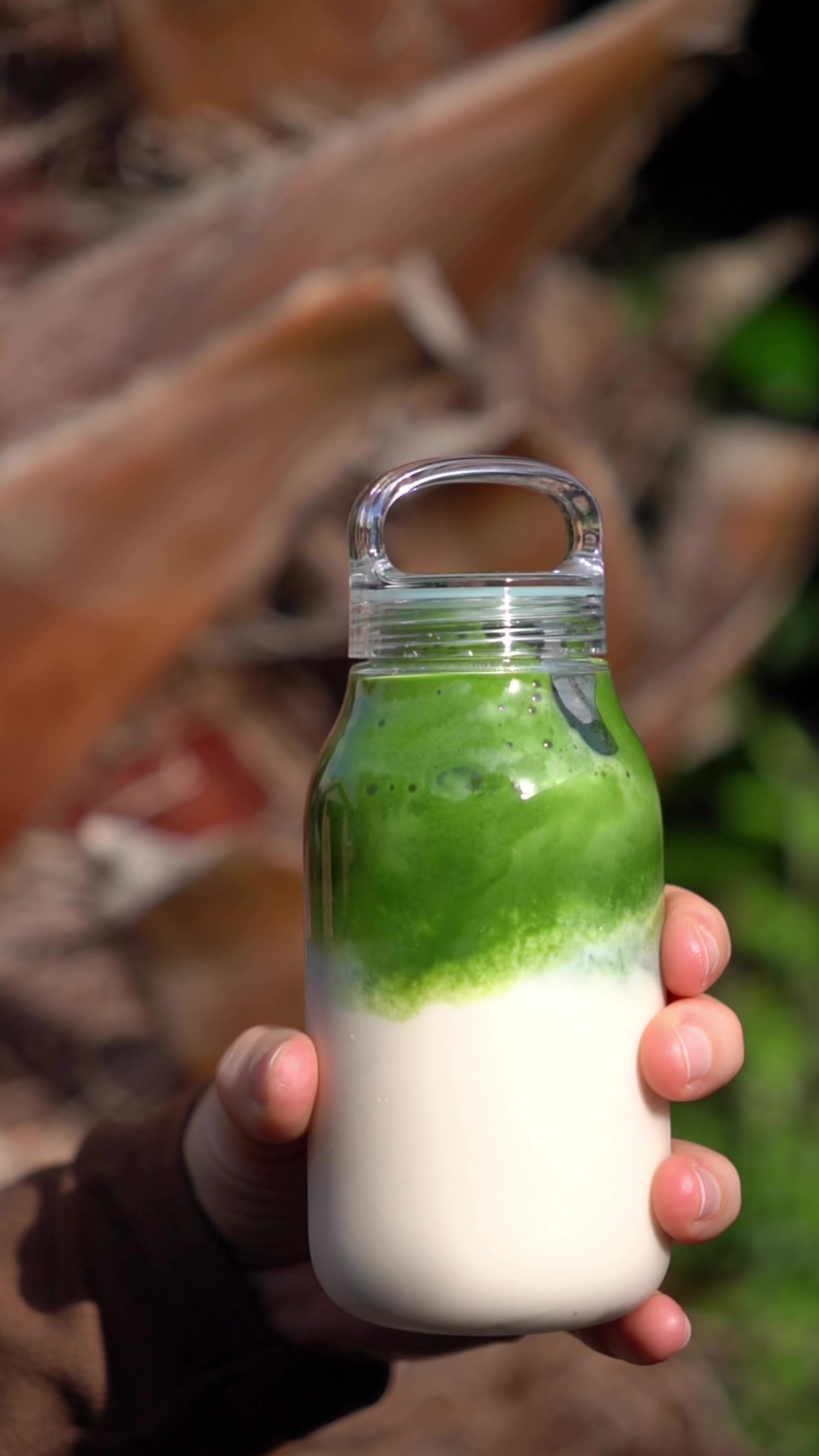 KINTO small clear plastic water bottle with matcha latte inside being shaken in slow motion.